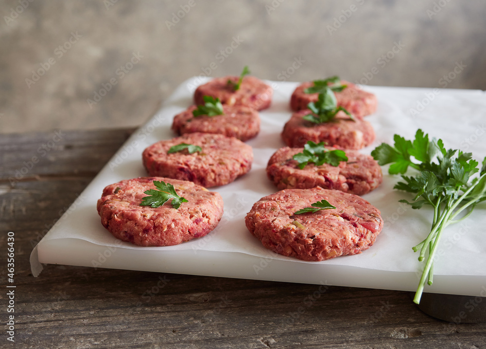 rows of freshly prepared homemade raw vegan burger patties placed on white parchment paper with parsley on top. Meat alternative.