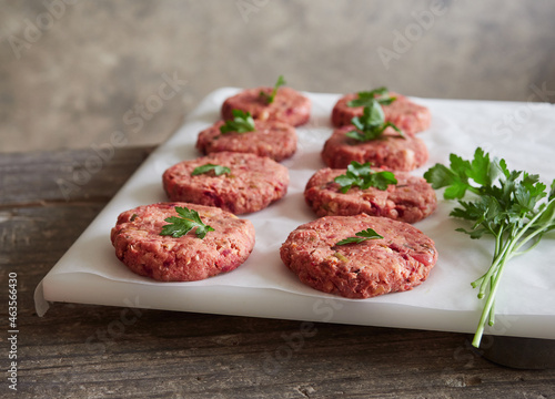 rows of freshly prepared homemade raw vegan burger patties placed on white parchment paper with parsley on top. Meat alternative.
