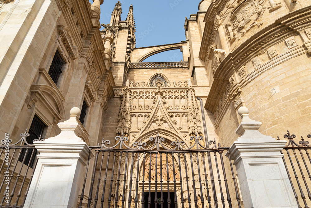 One of the entrance gates of the famous cathedral of Seville, Andalucia, Spain. Iron fence in the foreground. Blue sky in the background.
