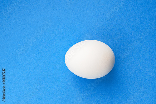 One white raw chicken egg in shell on a blue background. Breakfast ingredient. Product for Easter. Top view, flat lay.