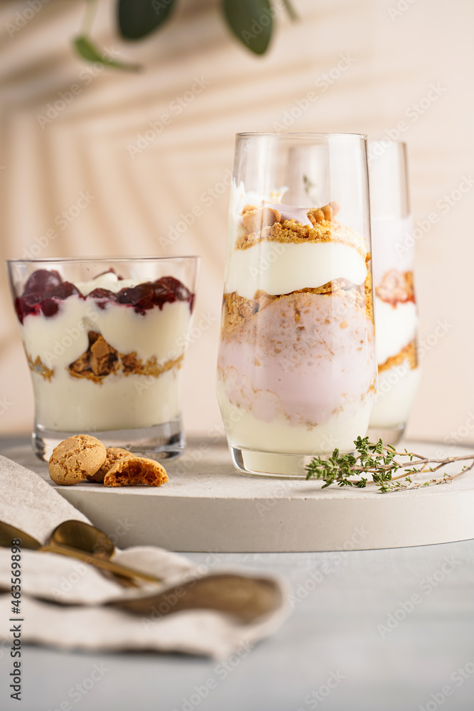 Three glasses with a layered creamy yoghurt dessert trifle with cookies, amaretti, cherries and thyme in a tropical setting Three glasses with a layered creamy yoghurt dessert trifle with cookies, amaretti, cherries and thyme in a tropical setting