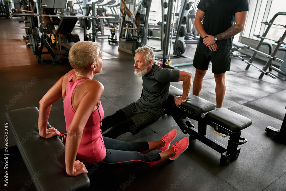Middle age woman excercising with male friend in gym - obrazy, fototapety, plakaty 