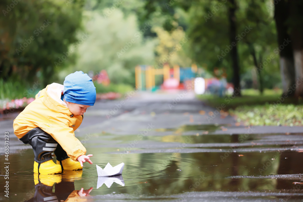 paper boat puddle game, boy seasonal autumn look raincoat, yellow rubber boots, outdoor game paper boat puddle game, boy seasonal autumn look raincoat, yellow rubber boots, outdoor game