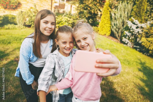 Group of happy teenage girls laughing and taking a selfie on a mobile phone outdoors.