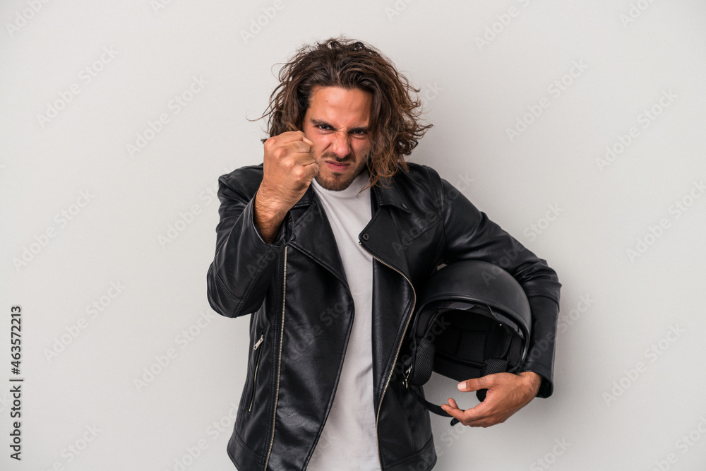 Young biker caucasian man holding a motorbike helmet isolated on gray background showing fist to camera, aggressive facial expression. Young biker caucasian man holding a motorbike helmet isolated on gray background showing fist to camera, aggressive facial expression.