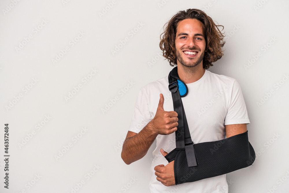 Young caucasian man with broken hand isolated on gray background smiling and raising thumb up Young caucasian man with broken hand isolated on gray background smiling and raising thumb up
