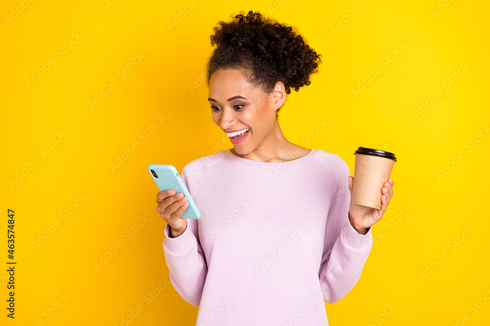 Photo of amazed shocked dark skin happy woman hold phone smile coffee isolated on yellow color background Photo of amazed shocked dark skin happy woman hold phone smile coffee isolated on yellow color background