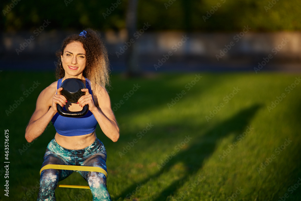 Fototapeta premium Caucasian woman personal trainer lifting heavy kettle with a treadmill on her knees
