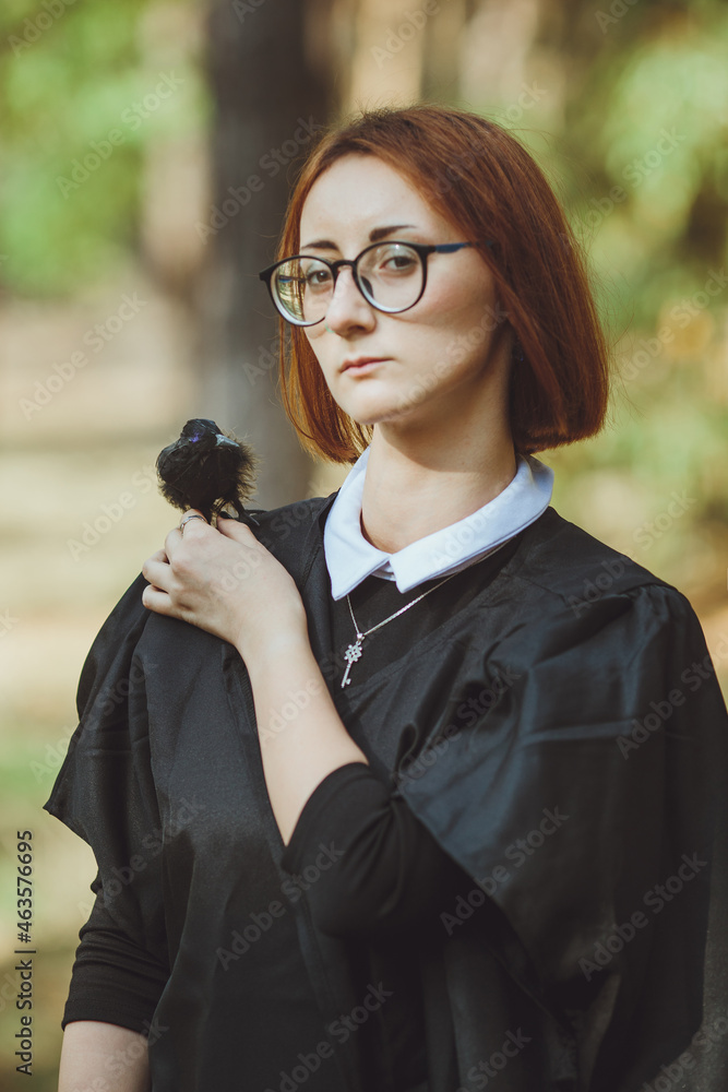 Halloween witch. Portrait of a girl in a hat and witch costume and with a black raven in the forest. Ready for the holiday wallet or life
