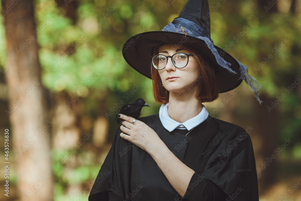 Halloween witch. Portrait of a girl in a hat and witch costume and with a black raven in the forest. Ready for the holiday wallet or life