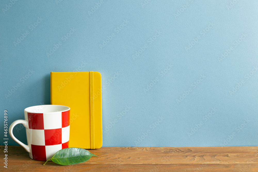 Yellow diary note book with mug cup on wooden desk. blue wall background