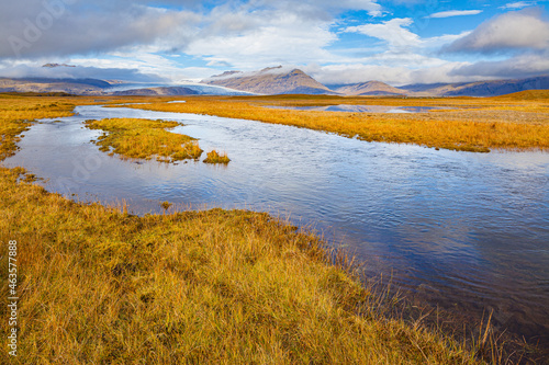 Landscape in south Iceland in autumn colors with a little stream and mountains with a glacier in the background