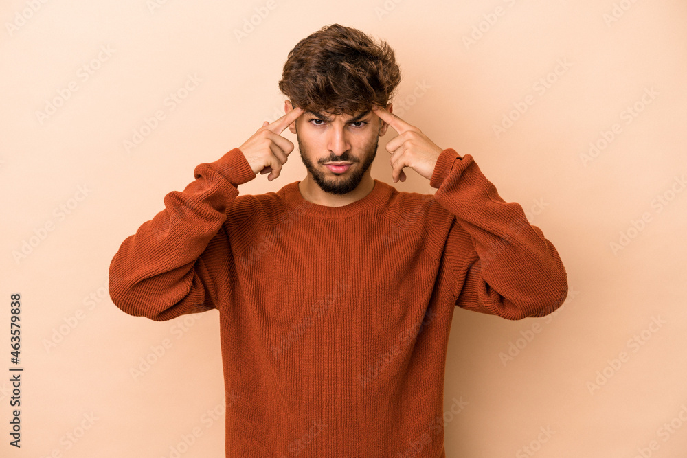 Young arab man isolated on beige background focused on a task, keeping forefingers pointing head. Young arab man isolated on beige background focused on a task, keeping forefingers pointing head.