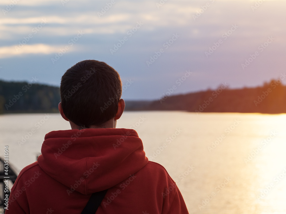 A man in an orange hoodie looks at a cloudy autumn sunset by the lake. Lifestyle, rest and freedom A man in an orange hoodie looks at a cloudy autumn sunset by the lake. Lifestyle, rest and freedom