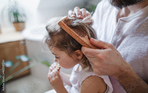 Canvas Print Unrecognizable father with small daughter indoors in bathroom at home, combing hair