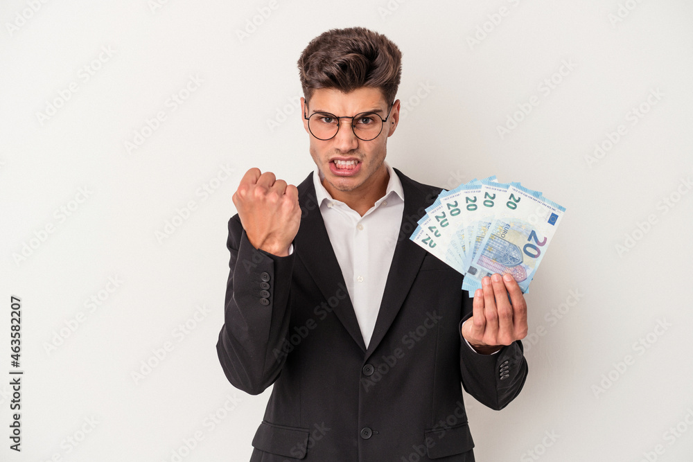 Young business caucasian man holding banknotes isolated on white background showing fist to camera, aggressive facial expression. Young business caucasian man holding banknotes isolated on white background showing fist to camera, aggressive facial expression.