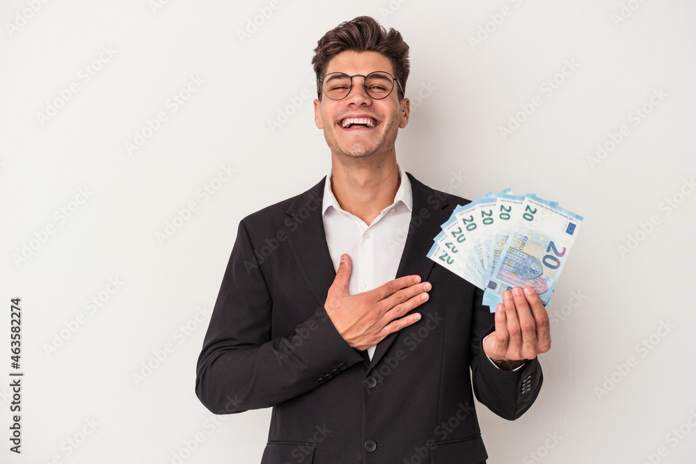 Young business caucasian man holding banknotes isolated on white background laughs out loudly keeping hand on chest. Young business caucasian man holding banknotes isolated on white background laughs out loudly keeping hand on chest.