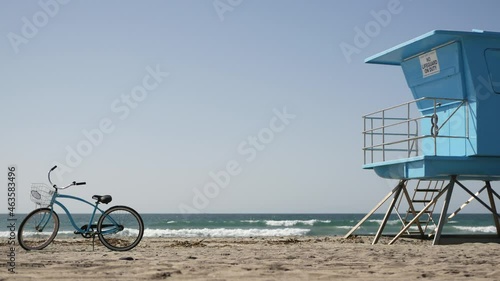 Blue bicycle, cruiser bike by ocean beach, pacific coast, Oceanside California USA. Summertime vacations, sea shore. Vintage cycle on sand near lifeguard tower or watchtower hut. Sky and water waves.