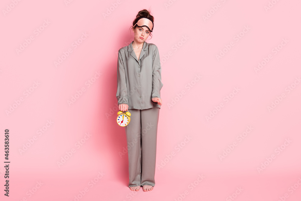 Full length body size view of attractive sad girl holding alarm clock wake up call isolated over pink pastel color background Full length body size view of attractive sad girl holding alarm clock wake up call isolated over pink pastel color background