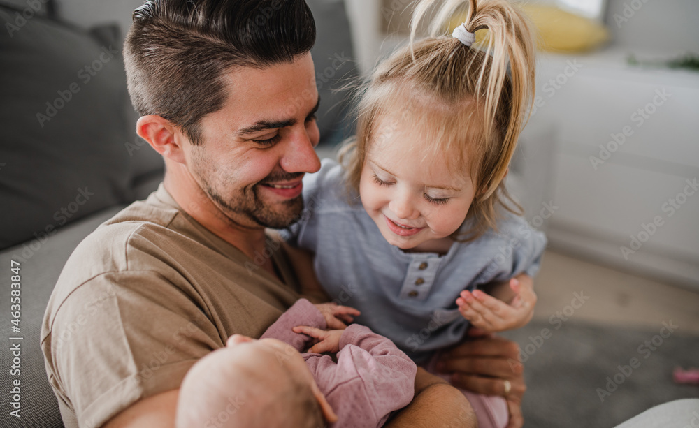 Happy young man taking care of his newborn baby and little daughter indoors at home, paternity leave Happy young man taking care of his newborn baby and little daughter indoors at home, paternity leave