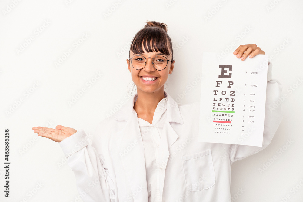Young mixed race optician woman doing a test isolated on white background showing a copy space on a palm and holding another hand on waist. Young mixed race optician woman doing a test isolated on white background showing a copy space on a palm and holding another hand on waist.