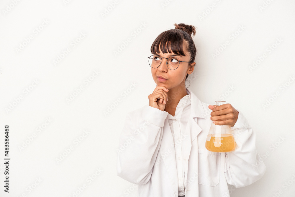 Young mixed race scientist woman holding a test tube isolated on white background looking sideways with doubtful and skeptical expression. Young mixed race scientist woman holding a test tube isolated on white background looking sideways with doubtful and skeptical expression.