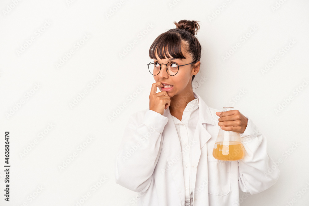 Young mixed race scientist woman holding a test tube isolated on white background relaxed thinking about something looking at a copy space. Young mixed race scientist woman holding a test tube isolated on white background relaxed thinking about something looking at a copy space.