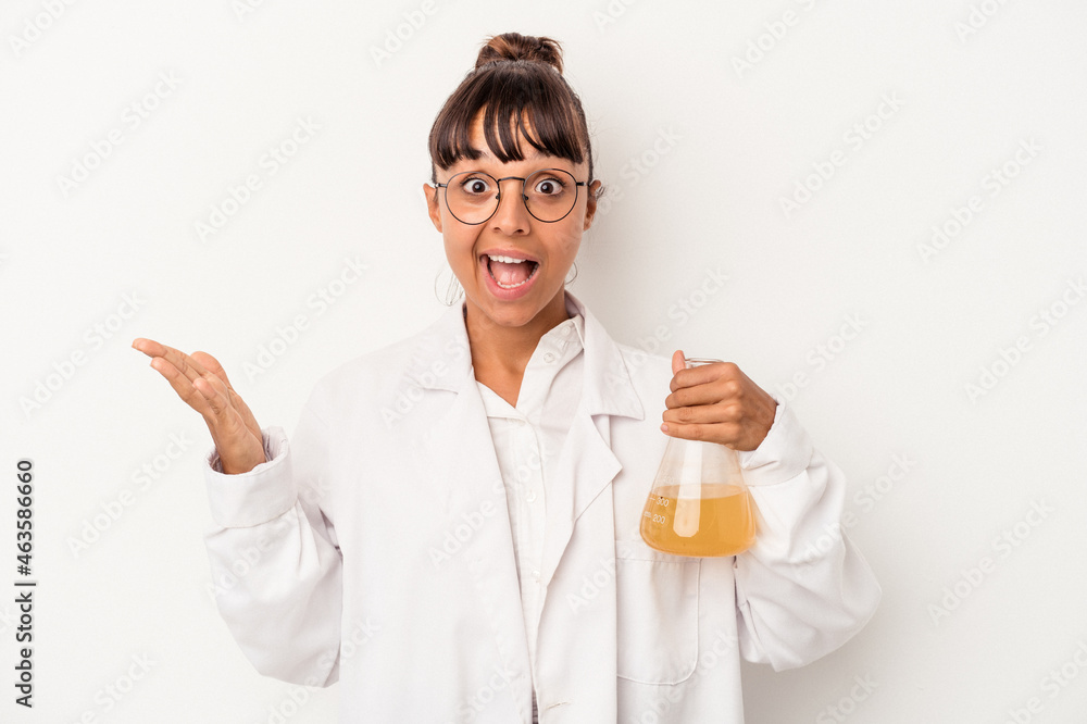 Young mixed race scientist woman holding a test tube isolated on white background receiving a pleasant surprise, excited and raising hands. Young mixed race scientist woman holding a test tube isolated on white background receiving a pleasant surprise, excited and raising hands.