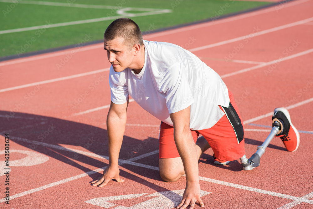 Fototapeta premium Caucasian male athlete with a prosthetic leg standing at the start on the track at the stadium. Sport concept.