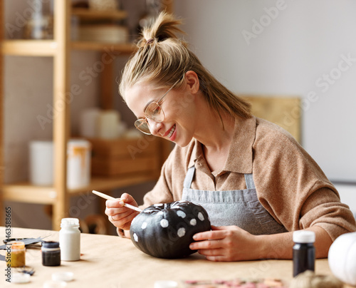 Woman in apron painting Halloween pumpkin with paint brush in hand