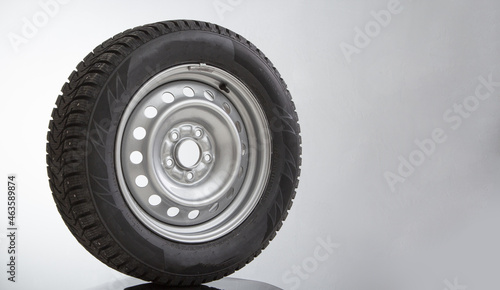 Car wheel and winter studded tire on grey background