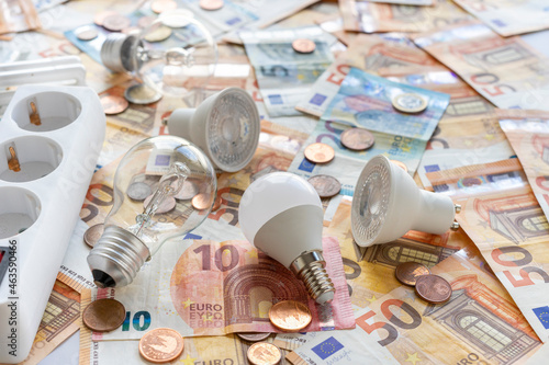 Electricity costs: Various types of light bulbs and electric socket on a background of euro banknotes and coins. . High quality photo