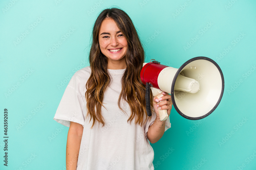 Young caucasian woman holding a megaphone isolated on blue background happy, smiling and cheerful. Young caucasian woman holding a megaphone isolated on blue background happy, smiling and cheerful.