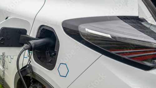 Close-up view of power supply plugged into an electric car being charged. White electric car charging.