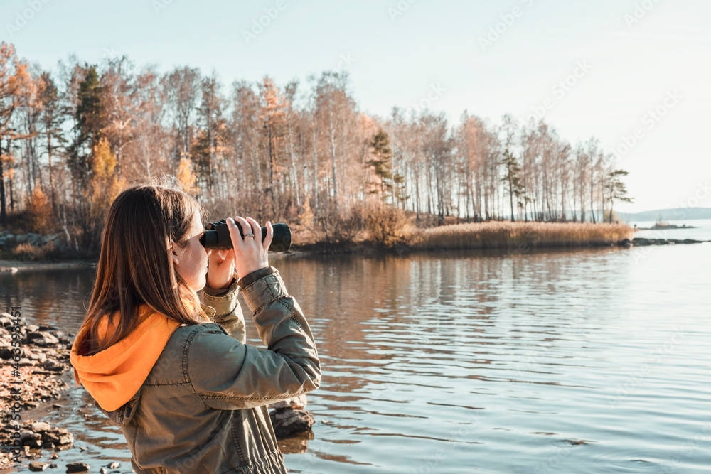 Young woman looking through binoculars at birds on lake Birdwatching, zoology, ecology. Research in nature, observation of animals. Ornithology autumn bird migration