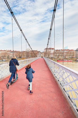Mother and her daugter riding scooters on the Old Passerelle du College bridge - Lyon, France