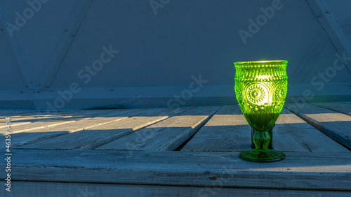 Illuminated empty glasses of green glass on a stem on a wooden background. Close-up view. © kalyanby