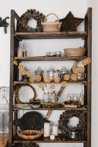 Cristmas decor of the kitchen interior with an old wooden open shelf, with dishes and garlands of orange pices