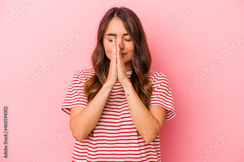 Young caucasian woman isolated on pink background holding hands in pray near mouth, feels confident. © Asier