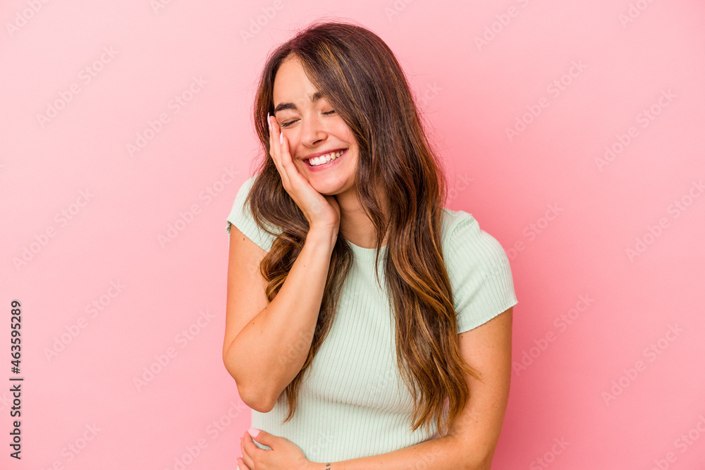 Fototapeta premium Young caucasian woman isolated on pink background laughs happily and has fun keeping hands on stomach.