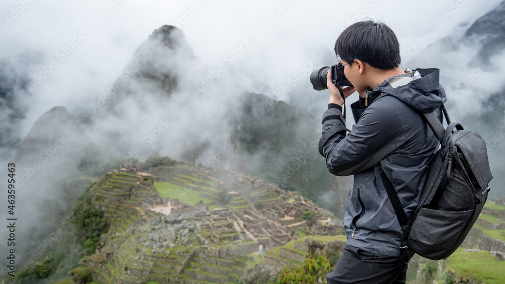 Asian man traveler and photographer taking photo at Machu Picchu, one of seven wonders and famous tourist attraction in Cusco Region of Peru. This majestic place has known as 'Lost City of the Incas'. Asian man traveler and photographer taking photo at Machu Picchu, one of seven wonders and famous tourist attraction in Cusco Region of Peru. This majestic place has known as 'Lost City of the Incas'.