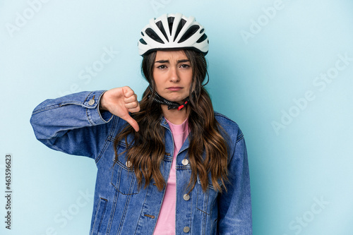 Young caucasian woman rinding a bike isolated on blue background showing a dislike gesture, thumbs down. Disagreement concept. © Asier