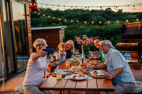 Canvas Print Happy senior woman and her cheerful family taking selfie during dinner in the ba