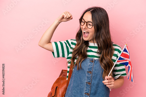 Young caucasian student woman studying English isolated on pink background raising fist after a victory, winner concept. photo