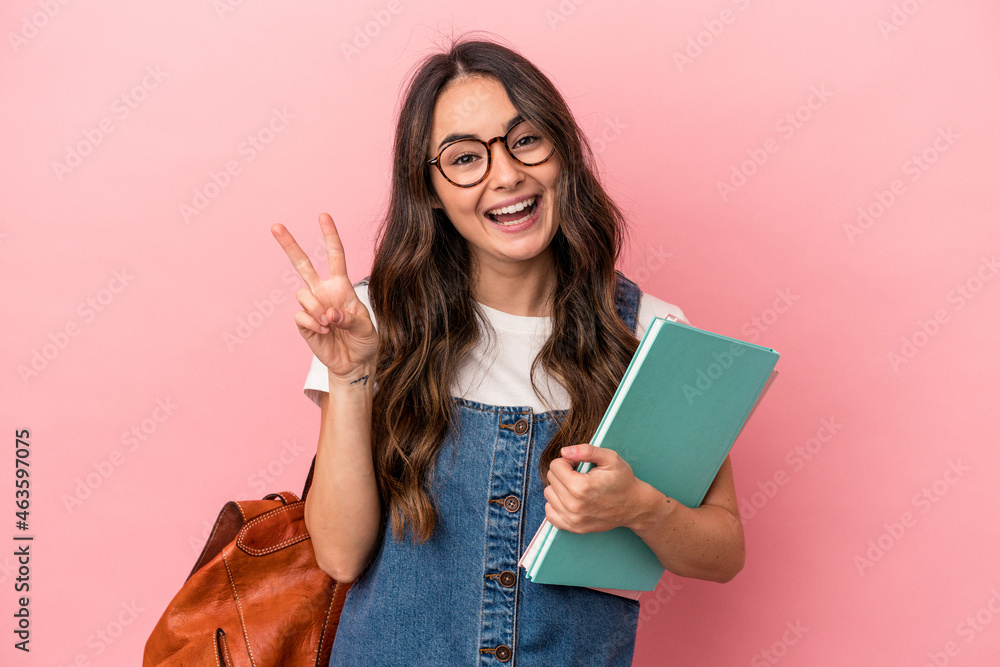 Young caucasian student woman isolated on pink background joyful and carefree showing a peace symbol with fingers. - obrazy, fototapety, plakaty 