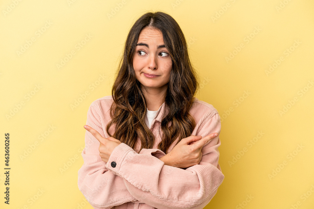 Young caucasian woman isolated on yellow background points sideways, is trying to choose between two options. Young caucasian woman isolated on yellow background points sideways, is trying to choose between two options.