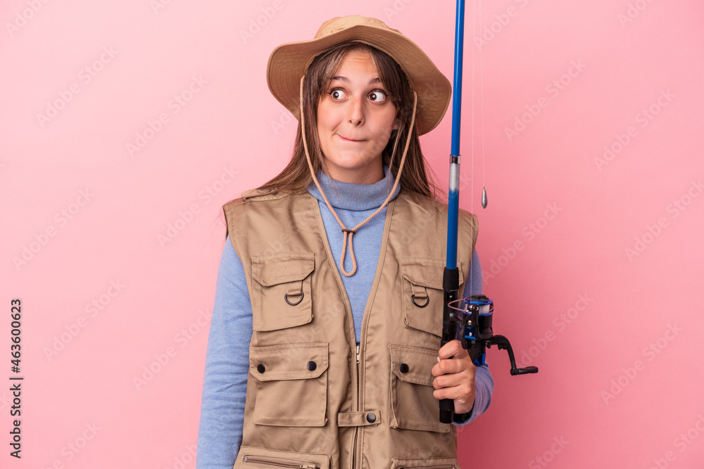 Young caucasian fisherwoman holding a rod isolated on pink background confused, feels doubtful and unsure. Young caucasian fisherwoman holding a rod isolated on pink background confused, feels doubtful and unsure.