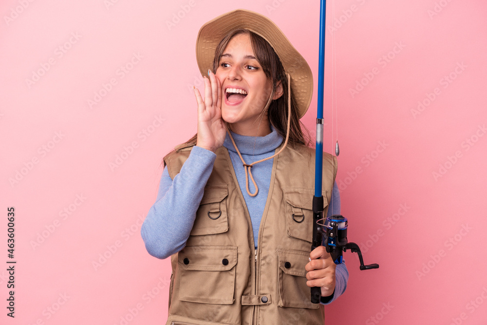 Young caucasian fisherwoman holding a rod isolated on pink background shouting and holding palm near opened mouth. Young caucasian fisherwoman holding a rod isolated on pink background shouting and holding palm near opened mouth.