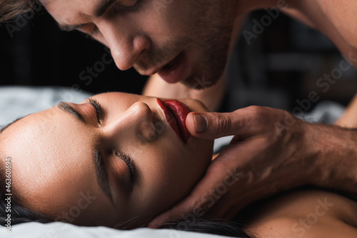Man touching sexy woman with closed eyes on bed on black background