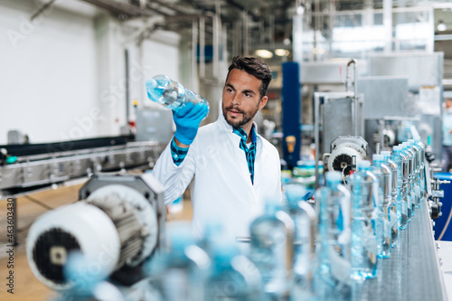 Male worker in bottling factory checking water bottles before shipment. Inspection quality control.